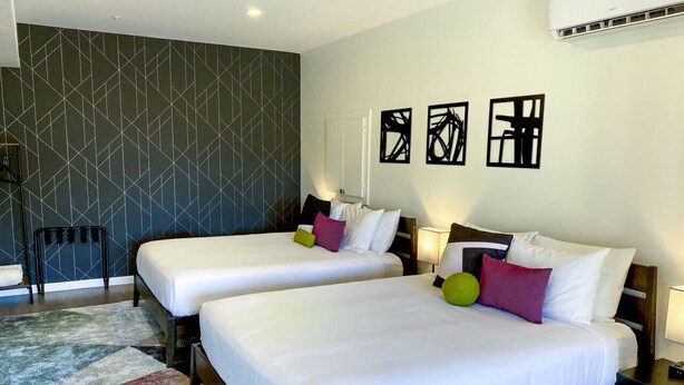 A hotel room with two beds, a chair, and a wall with abstract art.