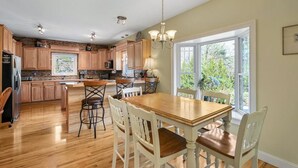 Una cocina amplia con armarios de madera, una isla central y un comedor con sillas blancas y una mesa de madera.