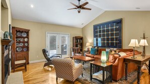 Un salón espacioso con ventilador de techo, chimenea, un ventanal y vistas al exterior.