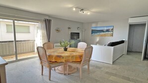 Ein Essbereich mit Tisch und Stühlen, einer kleinen Pflanze, einem Fernseher und einem Bild mit einer Strandansicht.