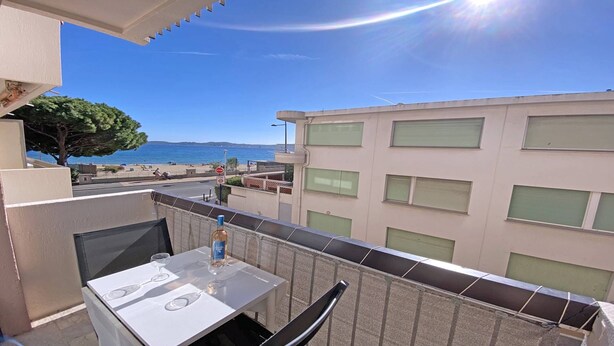 Ein Balkon mit Tisch und Stühlen, der Blick auf einen Strand und ein Gebäude mit vielen Fenstern bietet.