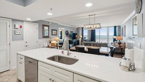 A modern kitchen with a large island, white cabinetry, and a view to the living area. - Oceanfront condo with full balcony - 2 blocks to shops & restaurants - COV 120! (Folly Beach)