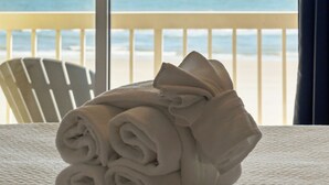 A neatly folded towel on a bed with a view of the ocean through large windows. - Oceanfront condo with full balcony - 2 blocks to shops & restaurants - COV 120! (Folly Beach)