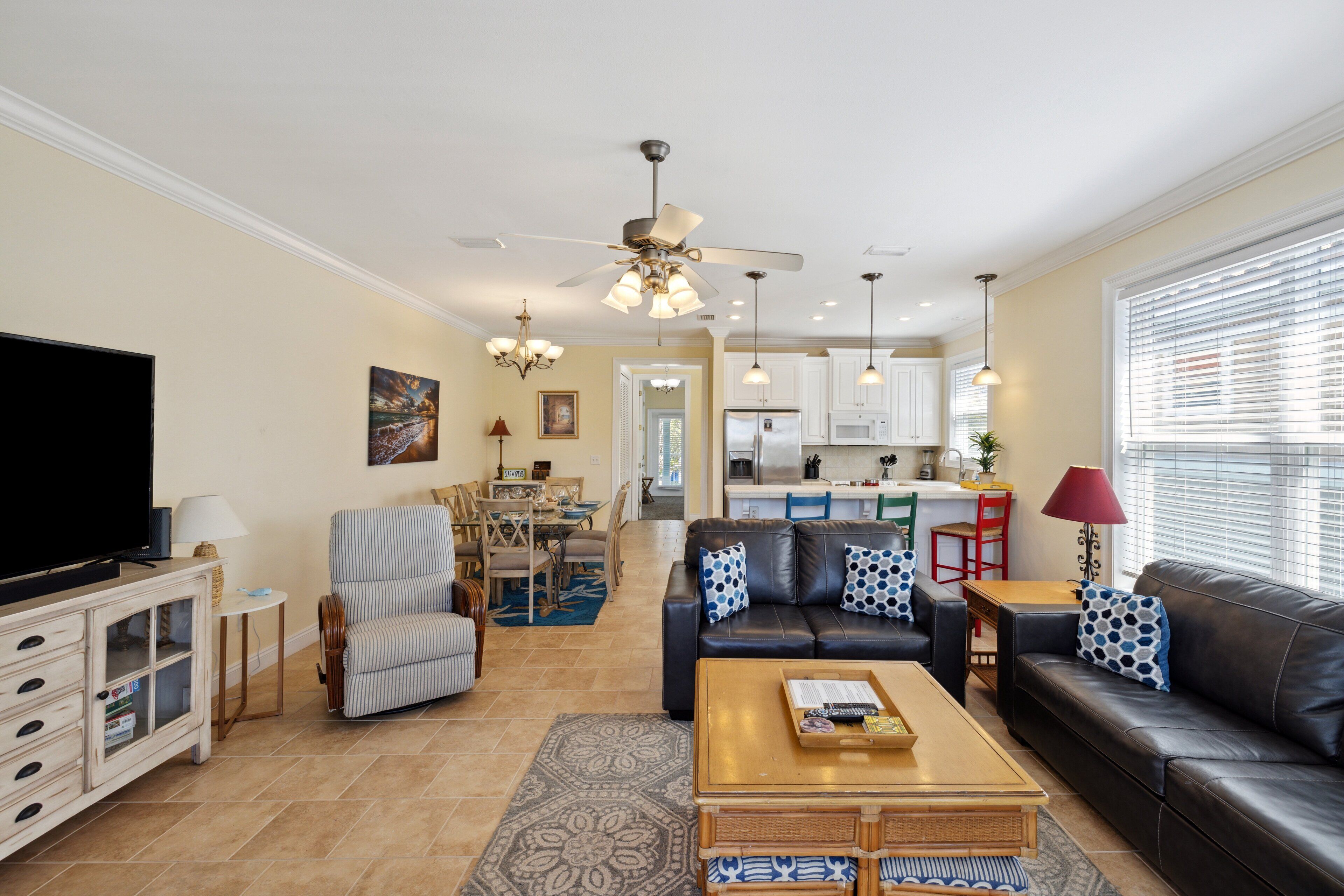 Una sala de estar moderna con un sofá, sillones, una mesa de centro y un televisor. Se observa un comedor con una mesa y sillas, y una cocina al fondo.