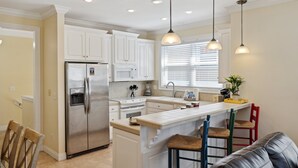 Una cocina moderna con armarios blancos, un refrigerador de acero inoxidable, horno empotrado e isla central con taburetes de bar.