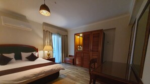A hotel room with a bed, a desk, a chair, a lamp, a wardrobe, and a window with curtains. - Kemet Boutique Hotel (Giza)