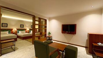 Habitación de hotel con cama, dos mesitas de noche con lámparas, televisor montado en la pared, una pequeña mesa con sillas y un armario de madera.