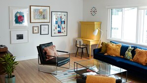 Ein modernes Wohnzimmer mit einem Glastisch, einem schwarzen Ledersessel, einem blauen Sofa und einem gelben Schreibtisch.