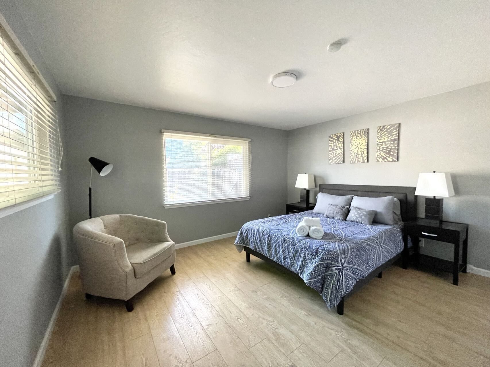 Une chambre à coucher avec un lit, une chaise, une table de chevet, une lampe et une fenêtre.