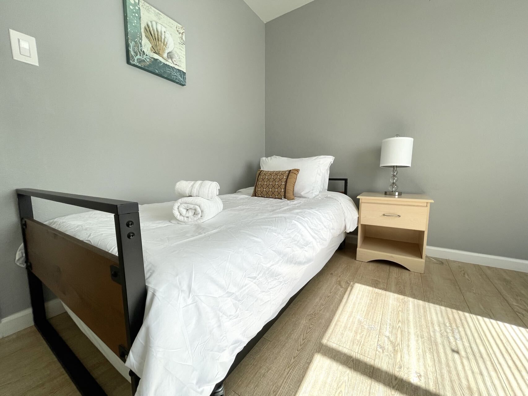 Une chambre à coucher avec un lit, une table de chevet, une lampe et un tableau accroché au mur.