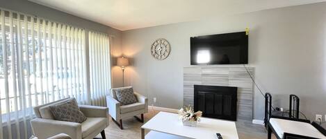 A modern living room with a sofa set, a coffee table, a fireplace, and a flat-screen TV mounted above it.