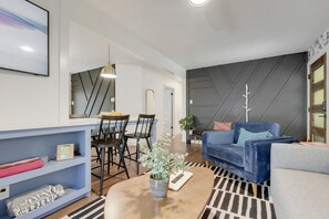 A modern living room with a blue sofa, a coffee table, and a dining area with chairs and a table.