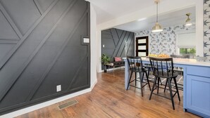 A modern kitchen with a black geometric wall, wooden flooring, and a blue island with bar stools.