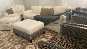 A living room with a patterned carpet, a white sofa with patterned cushions, a zebra-striped armchair, and a matching ottoman. - Fireplace and Farmers Market Cozy! (Dubuque)