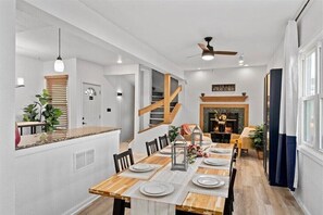 Un espace repas moderne avec une table en bois dressée pour six personnes, un escalier et une cheminée.