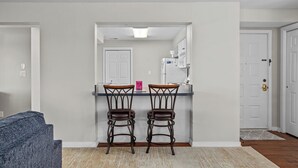 A kitchen with two bar stools, a refrigerator, and a white door.