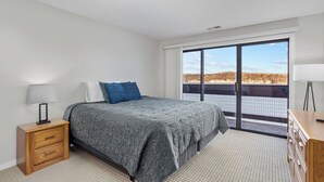 A bedroom with a bed, a nightstand, a dresser, and a large window with a view.