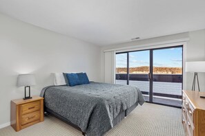 Un dormitorio con cama, mesita de noche, cómoda y una ventana grande con vistas.