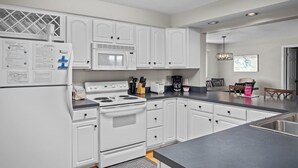 A modern kitchen with white cabinetry, a built-in microwave, stove, and oven. There is a dining area with a table and chairs, and a kitchen island with a sink.