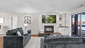 A modern living room with a fireplace, grey sofas, a rug, and a view of a lake through large windows.
