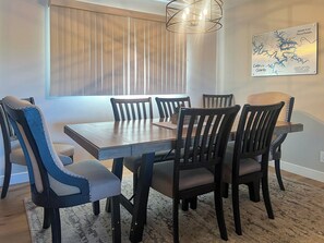 Een eethoek met een houten tafel, zes stoelen, een hanglamp en een aan de muur bevestigde kaart.