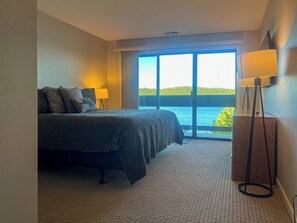 Een hotelkamer met een bed, twee bedlampen, uitzicht op zee en een balkon met een hekwerk.
