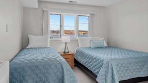 A bedroom with two beds, a nightstand, a lamp, and a window with a view of the outdoors.