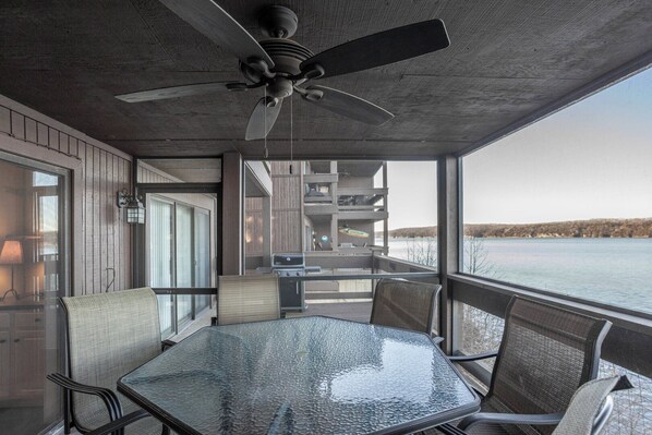 An outdoor deck with a glass table and chairs, a ceiling fan, and a view of a lake.