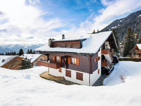 Un bâtiment de style chalet, avec une façade en bois, un balcon et un toit recouvert de neige.