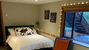 A bedroom with a bed, a chair, a window with a view of a staircase, and wall-mounted lights.