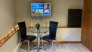 A small meeting room with a glass table, two black chairs, a TV on the wall, and a wooden cabinet.