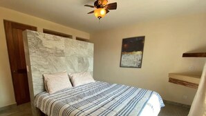 A bedroom with a bed, a ceiling fan, a night sky painting, and a wooden headboard. - Amazing private beachfront Village (Troncones)
