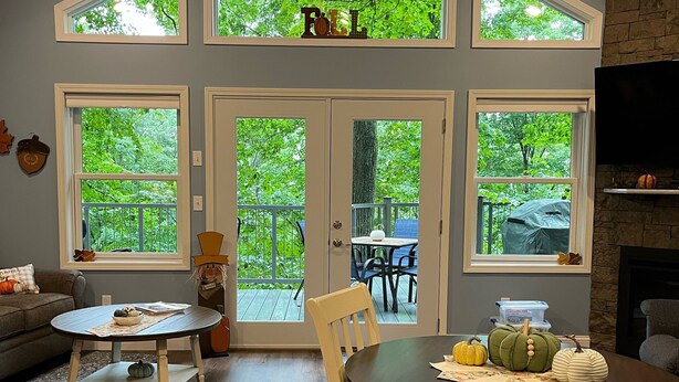 Ein Essbereich mit Tisch und Stühlen, große Fenster mit Blick auf Bäume und ein Kamin.