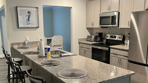 Cozinha moderna com ilha central, eletrodomésticos de aço inoxidável e parede com detalhes em azul.