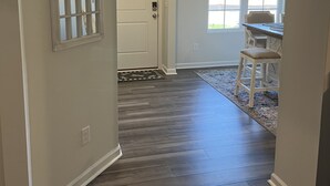 Um corredor com piso de madeira, uma porta com janela decorativa e uma janela com persianas.