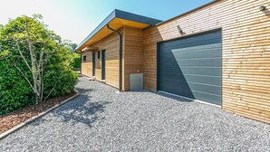 A modern building with a wooden facade, a garage door, and a gravel driveway. - Maison BOOA 4* - Private swimming pool & Lake nearby (Sévrier)
