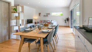 A modern dining area with a wooden table, grey chairs, and a glass-top dining table. There is a sofa and a TV in the background. - Maison BOOA 4* - Private swimming pool & Lake nearby (Sévrier)