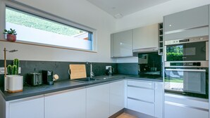 A modern kitchen with white cabinets, a black countertop, and a built-in oven. - Maison BOOA 4* - Private swimming pool & Lake nearby (Sévrier)
