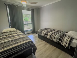 A bedroom with two beds, a ceiling fan, and a window with curtains.