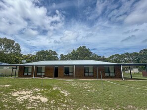 A single-story brick building with a metal roof, surrounded by a grassy area and trees.