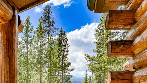 Una cabaña de madera con un balcón que da a un bosque y montañas.