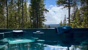 Tinaja exterior con agua cristalina, rodeada de altos pinos y una vista de la montaña al fondo.