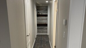 Un estrecho pasillo con suelo de madera oscura, paredes blancas y una pared central de madera decorativa.