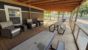 Un espacio de estar techado al aire libre con mobiliario de mimbre, una mesa de picnic y vistas a un parque.