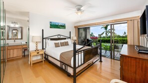 Un dormitorio moderno con una cama grande, un escritorio y un balcón con vistas a palmeras.