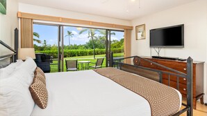 Habitación de hotel con cama, televisión, balcón y vista a zonas verdes, además de ventilador de techo.