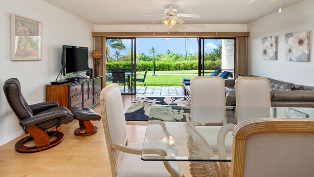Una sala de estar con una mesa de centro de vidrio, un sillón de cuero y un televisor sobre un mueble de madera.