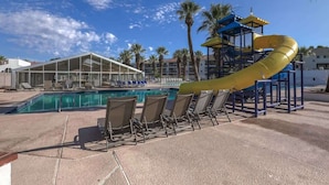 A pool area with a yellow slide, lounge chairs, and a covered seating area.