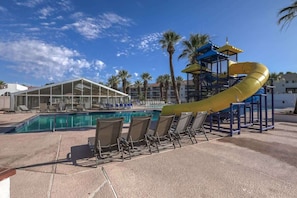 A pool area with a yellow slide, lounge chairs, and a covered seating area.