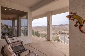 A balcony with a view of a desert landscape, a lizard decoration, and a row of chairs.